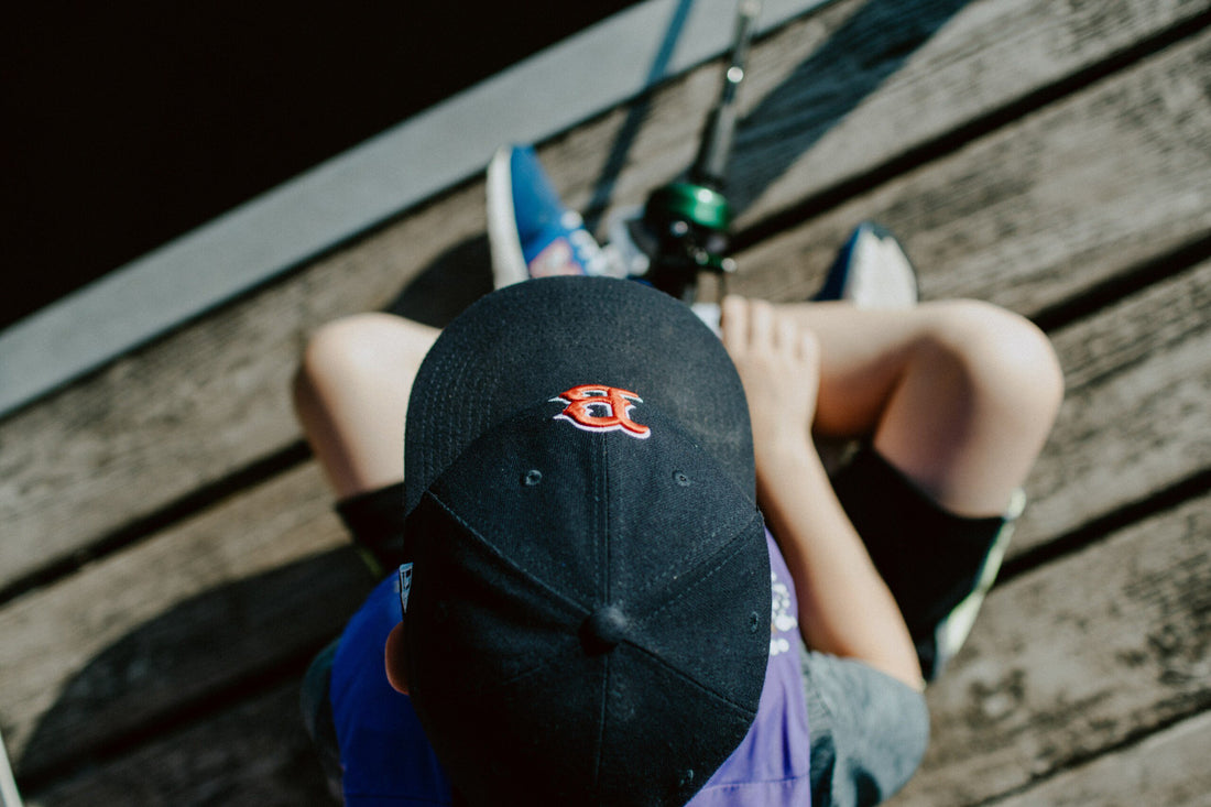 Boy from above sitting on a dock with a fishing rod.