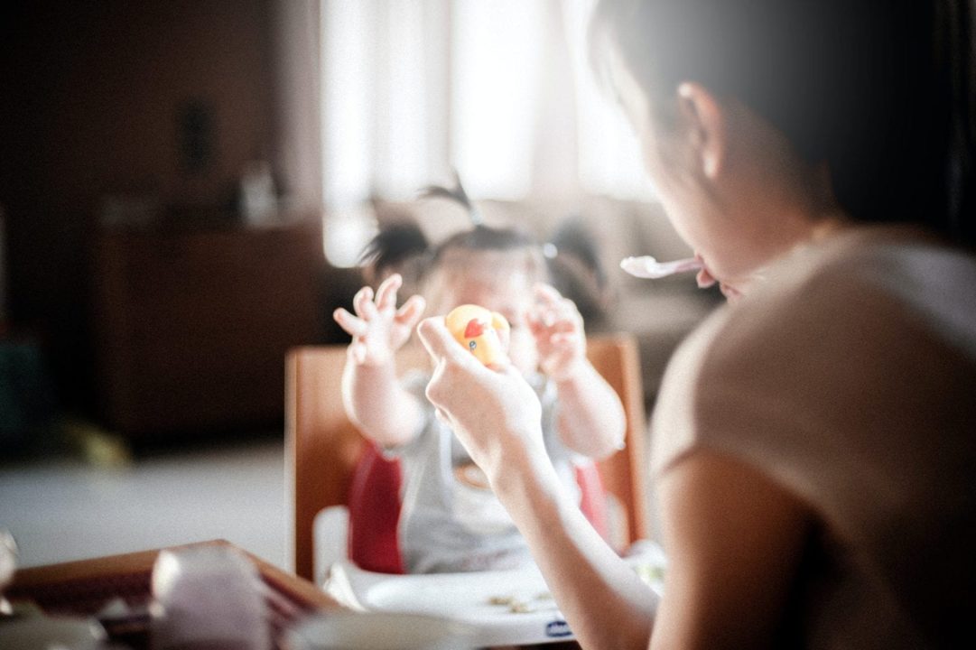 Women feeding her child in highchair while holding rubber ducky