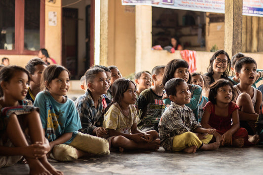 A group of children sitting on a floor listening to a speaker.