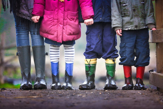 The bottom half of four children holding hands in rain boots