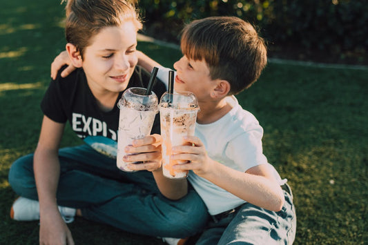 Two kids drinking out of a plastic cup and saying cheers