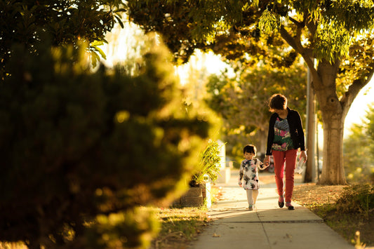 A mother and child walking down a sidewalk holding hands