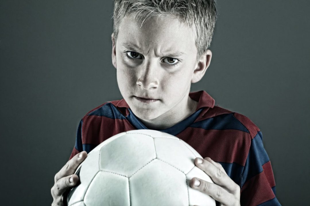 Angry child in red and blue shirt holding a ball