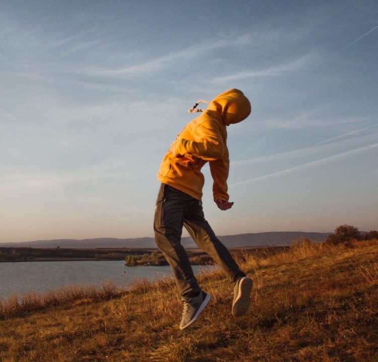 Child in yellow hoodie leaping into the air on grassy field