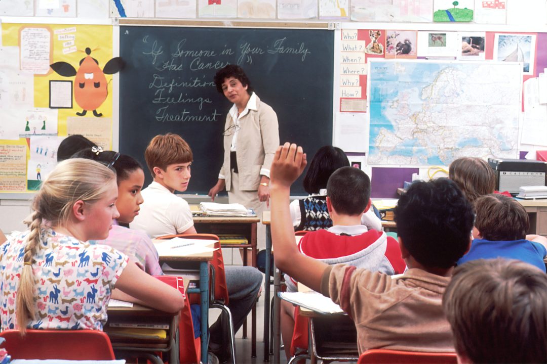 Teacher standing in front of a chalkboard teaching her class