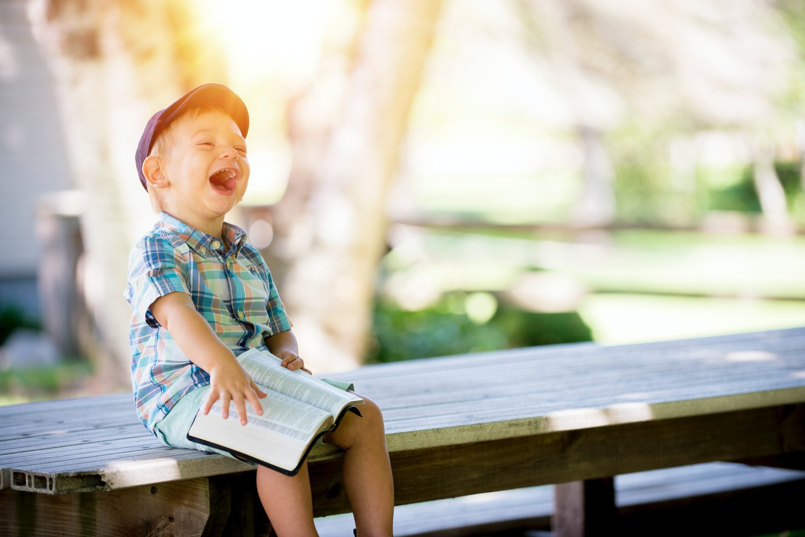 Child sitting on a bench with a book laughing