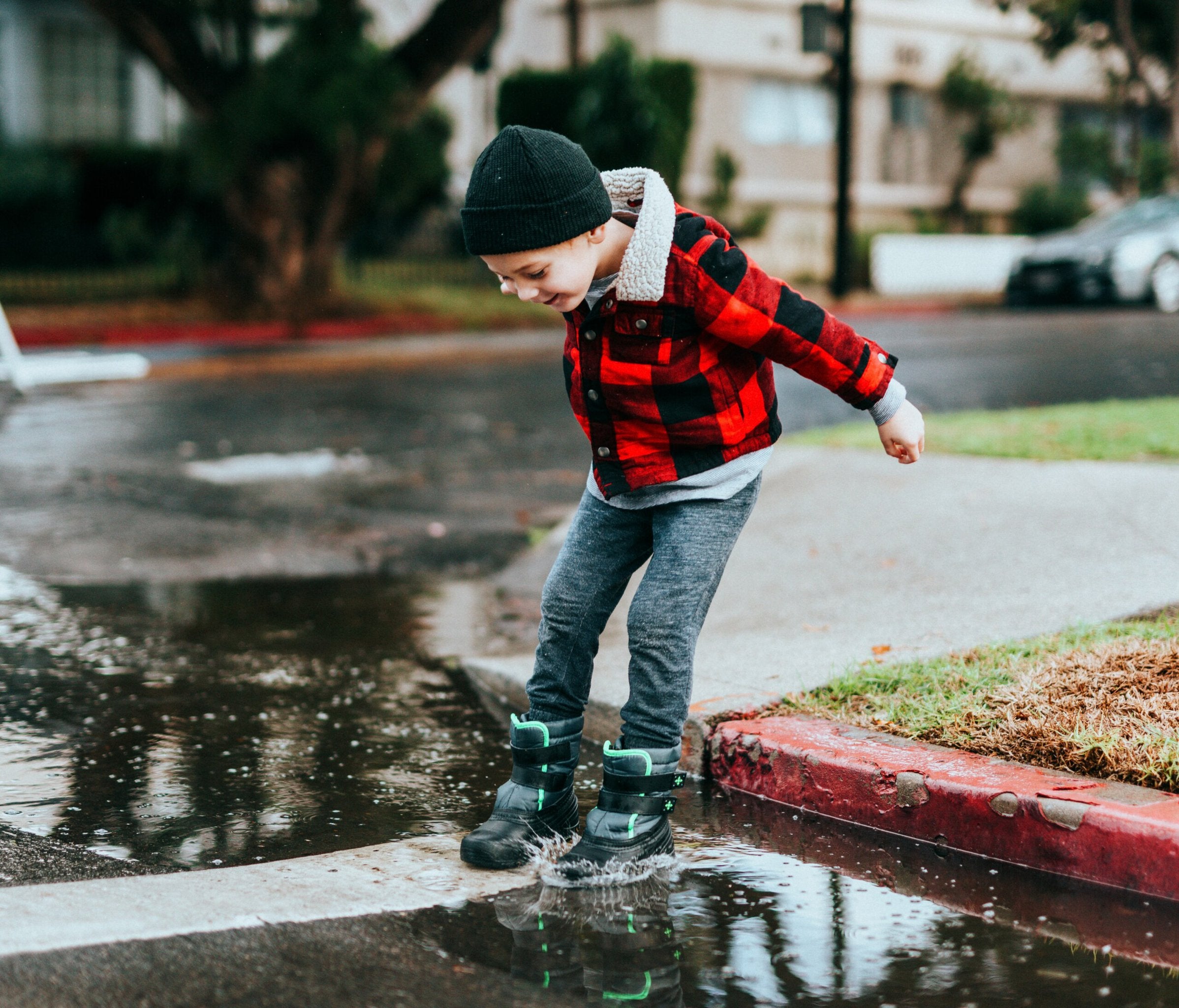 Child in red jacket jumping into a puddle