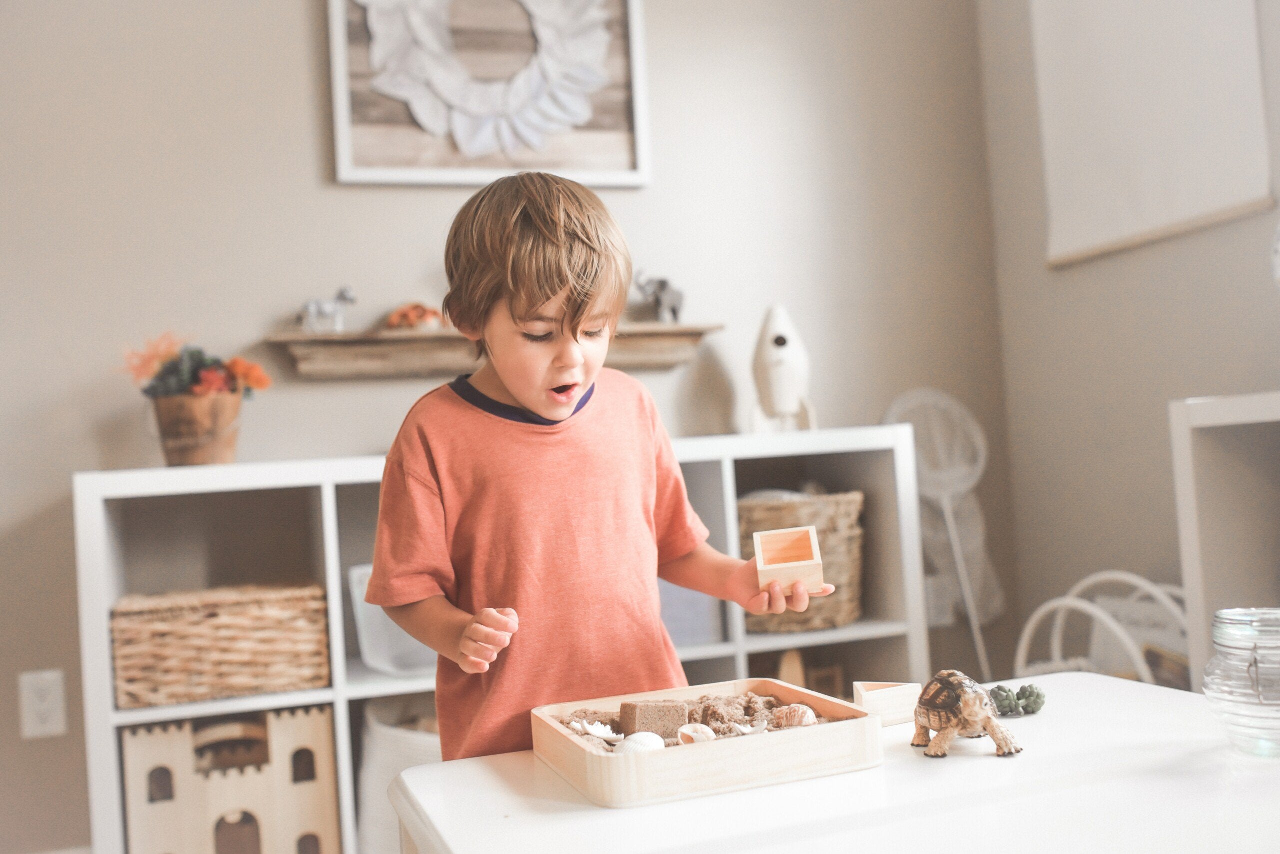 Boy in orange shirt at home looking through box of shells.